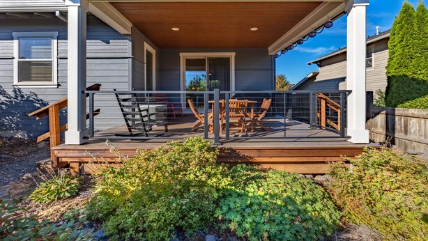 A covered deck with outdoor furniture, a wooden railing, and a view of the house.