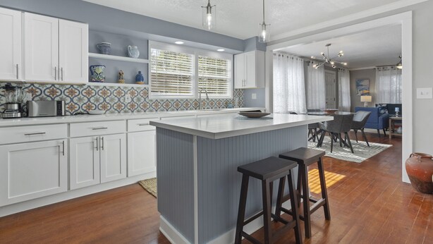 Una cocina moderna con armarios blancos, una isla azul e iluminación colgante.