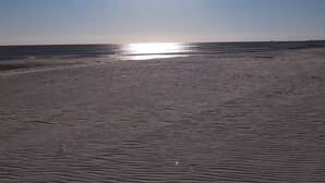 Una playa con el sol brillando directamente arriba, proyectando un reflejo intenso sobre la arena.
