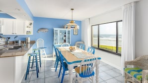 A kitchen with white cabinets, a blue wall, and a dining area with a table and chairs. - Errol by the Sea unit 125- 2BD - Beachy Keen (New Smyrna Beach)