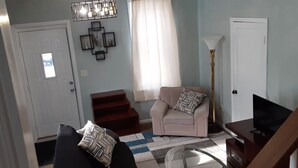 Un salon comprenant un canapé, un fauteuil, un téléviseur et un escalier menant à une autre pièce.