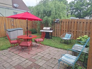 A backyard patio with a red umbrella, a grill, and outdoor furniture.
