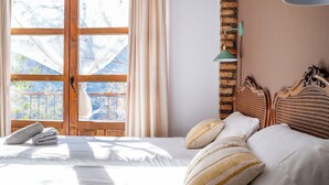 A hotel room with a large window, a bed with white linens, and a brick accent wall. - Almez De Lúa Güéjar Sierra by Ruralidays (Granada)