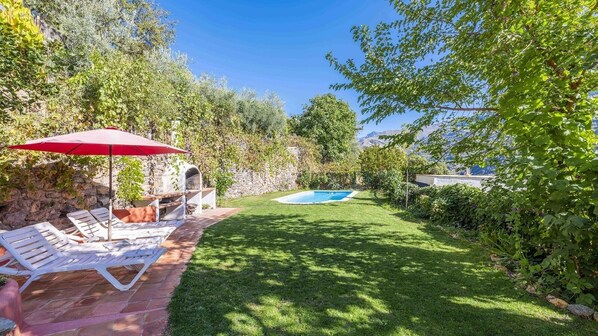 A backyard with a swimming pool, a barbecue area, and a patio with lounge chairs.
