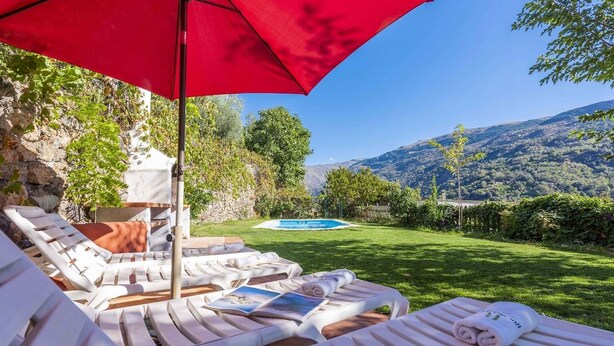 A poolside area with lounge chairs and a red umbrella, a clear view of a pool, and a mountainous landscape in the background. - Almez De Lúa Güéjar Sierra by Ruralidays (Granada)
