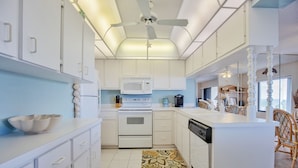 A modern kitchen with white cabinets, a microwave, an oven, and a dishwasher. There is a decorative rug on the floor and a ceiling fan. - Errol by the Sea unit 412- 1BD - Tide Time (New Smyrna Beach)
