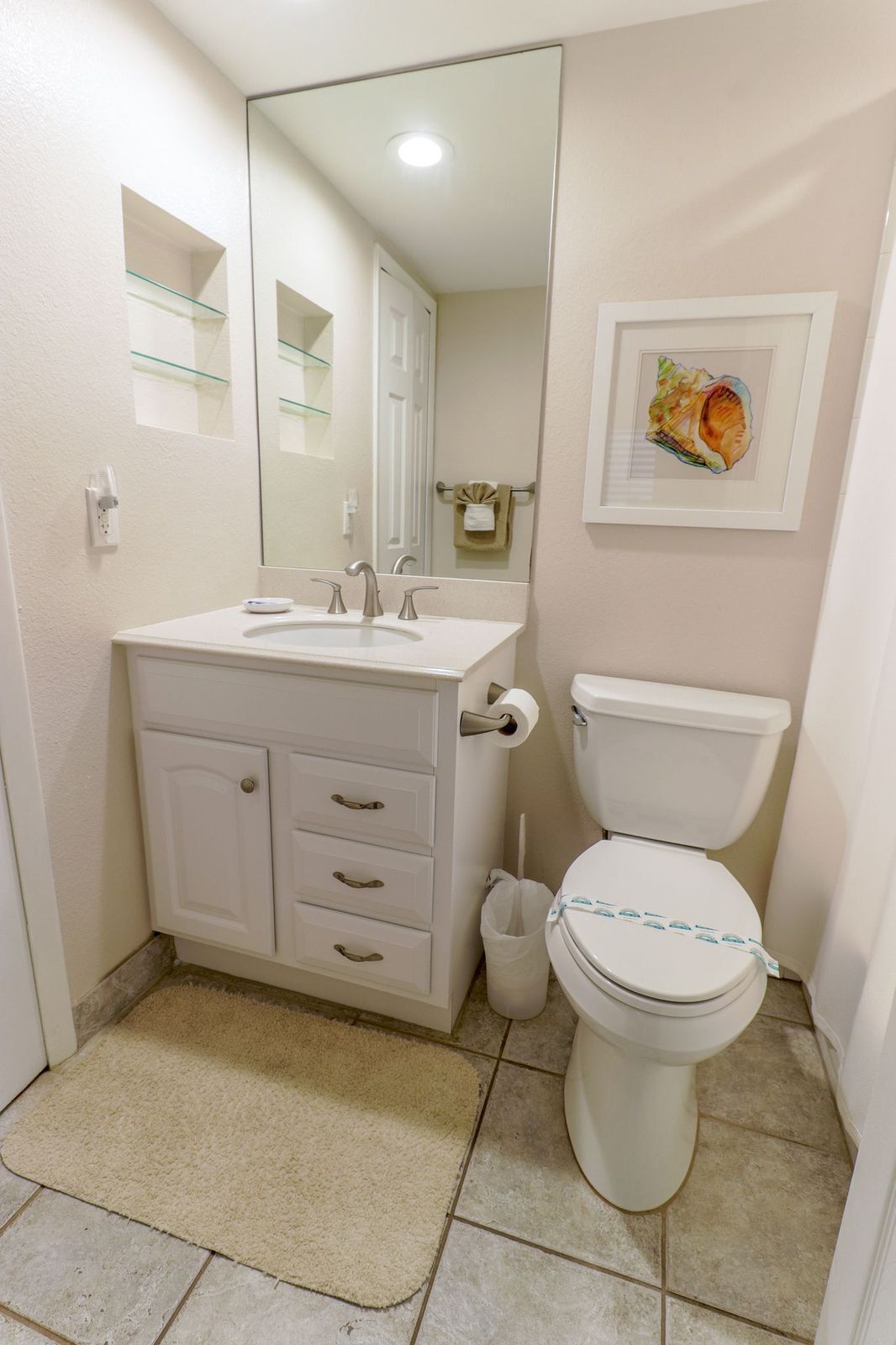 A bathroom with a white vanity, a toilet, a mirror, and a framed picture on the wall.
