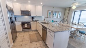 Cocina compacta con armarios blancos, refrigerador de acero inoxidable, microondas y lavavajillas. Hay una pequeña isla con un lavamanos y una mesa de comedor con sillas.