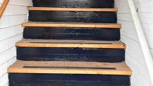 Una escalera de madera con escalones negros y barandal de madera, que sube.
