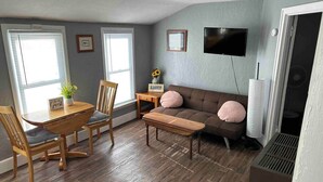 Una habitación con una mesa de comedor, sillas, un sofá y un televisor montado en la pared.