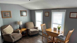 Una sala de estar acogedora con una mesa de comedor de madera, dos sillones, un sofá y una mesita auxiliar con una lámpara.