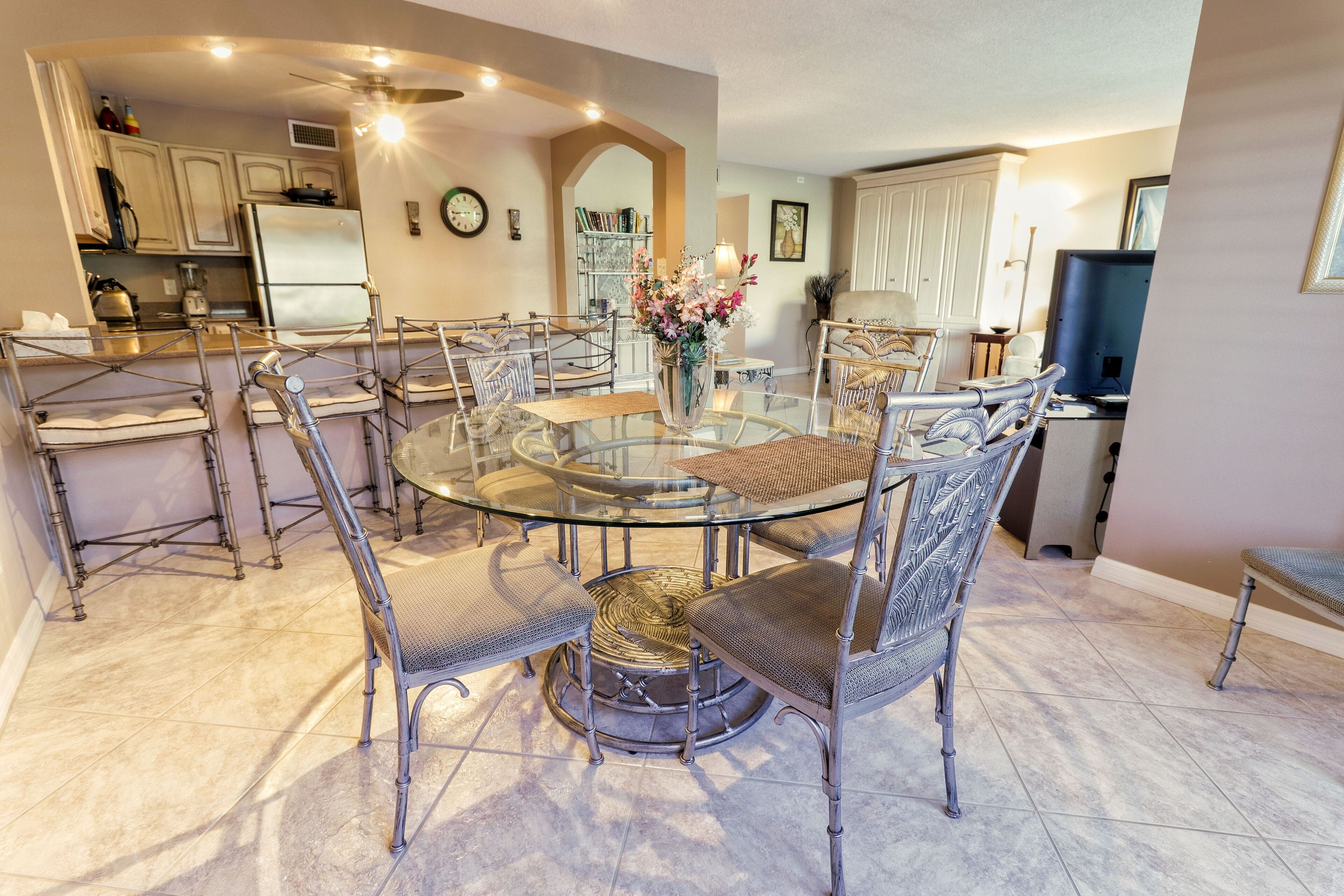 A modern kitchen with a central island, stainless steel appliances, and a dining area with a glass table and metal chairs.