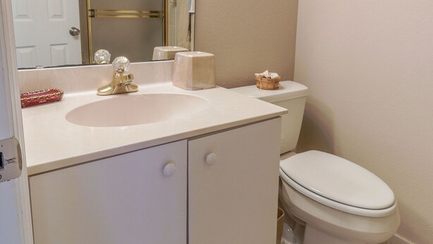 A bathroom with a white sink, a toilet, and a mirror. - Errol by the Sea - Unit 107 - 1BD - The Salty Nest (New Smyrna Beach)