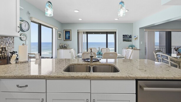 A kitchen with a large island, stainless steel sink, and overhead pendant lights.