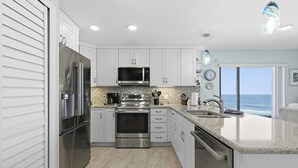 A modern kitchen with stainless steel appliances, white cabinets, and a view of the ocean.