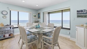 A dining area with a glass table and wicker chairs, overlooking the ocean.