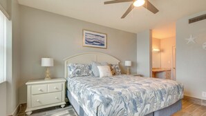 Ein Schlafzimmer mit Bett, Nachttischen, Deckenventilator, einem gerahmten Bild und einer Badezimmertür.