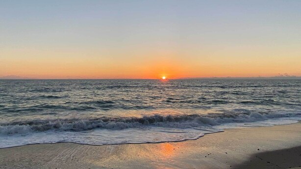 Ein Strand mit Wellen und einem Sonnenuntergang.