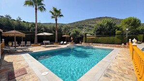 A rectangular pool with clear blue water, surrounded by stone tiles, palm trees, and lounge chairs. - La Torna Carcabuey by Ruralidays (Córdoba)