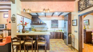 A kitchen with a central island, wooden chairs, a dining table, and a TV in the background. - La Torna Carcabuey by Ruralidays (Córdoba)