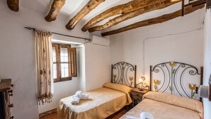 Een slaapkamer met twee bedden, houten balken in het plafond, een raam met gordijnen en een nachtkastje met een lamp.
