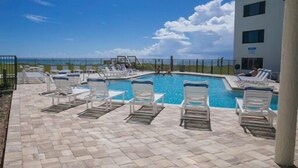 A pool area with lounge chairs and a view of the ocean.