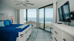 A bedroom with a bed, a TV, a desk, and a view of the ocean.