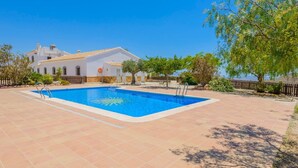 A swimming pool with a tiled deck, surrounded by a fence, and a building with a white facade and a red roof in the background. - Sol de Taberno - Ático Tía Beba by Ruralidays (Almería)
