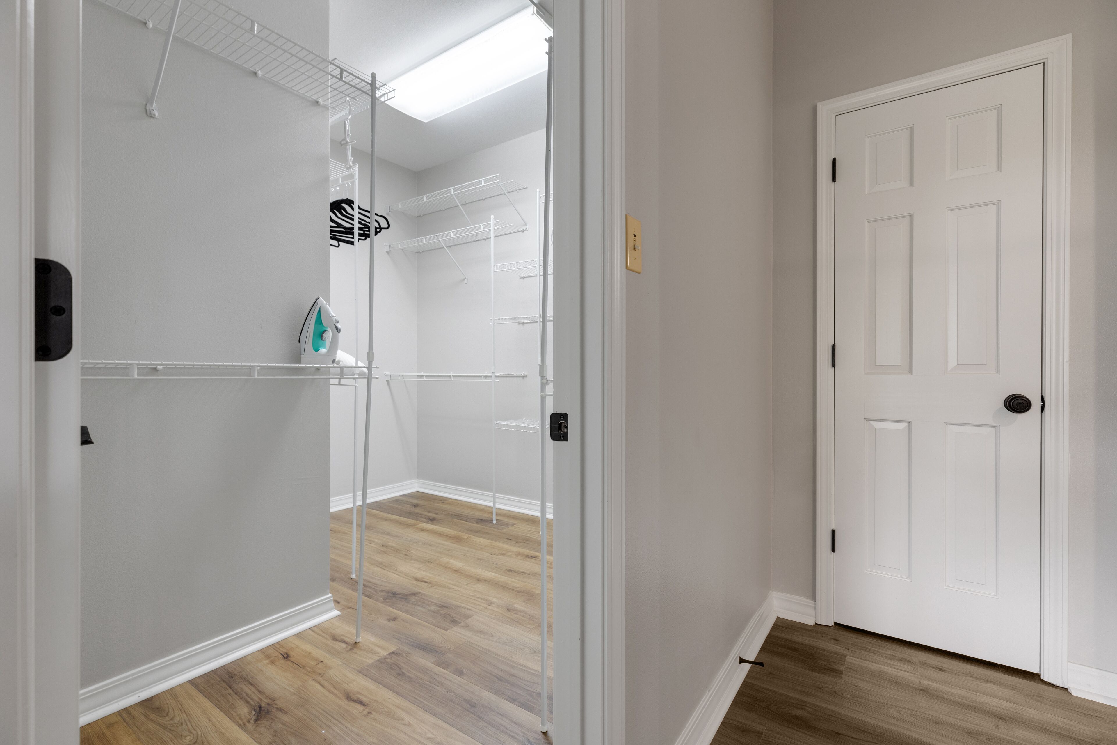 Un vestidor con estantes abiertos, una barra para colgar ropa y una puerta que da a otra habitación.