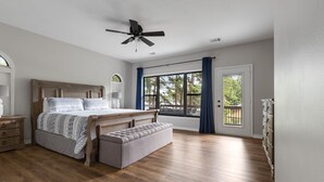 A bedroom with a wooden bed, a bench, a ceiling fan, and a large window with curtains.
