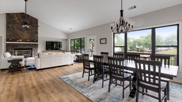 A spacious living area with a stone fireplace, a dining table with chairs, and a large window offering a view of the outdoors.