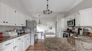 A modern kitchen with white cabinets, granite countertops, stainless steel appliances, and a chandelier.
