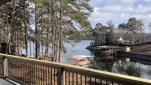 A lakeside view from a balcony with a wooden railing, dock, and docked boat.