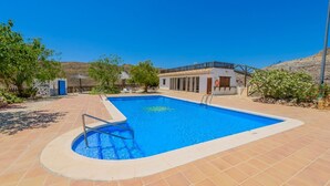 Una piscina rectangular con un borde de baldosas, un espacio pequeño junto a la piscina con una silla, y un edificio con un balcón al fondo.