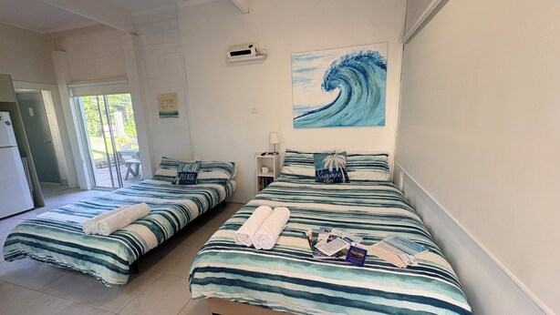 A room with two beds, a beach-themed painting, and a sign on the door. - Jones Beach Haven Studio Escape Kiama Downs opposite patrolled beach and park (KIAMA DOWNS)