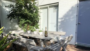 A wooden outdoor table with chairs, potted plants, and a bottle of champagne. - Jones Beach Haven Studio Escape Kiama Downs opposite patrolled beach and park (KIAMA DOWNS)
