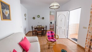 A living room with a sofa, a dining table with chairs, a wicker chair, a small table, and a door leading to a balcony. - Casas María Carmona - Casa Tierra Níjar by Ruralidays (Almería)