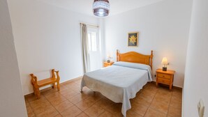 A bedroom with a bed, two bedside tables, a nightstand, a bench, and a window with curtains. - Casas María Carmona - Casa Tierra Níjar by Ruralidays (Almería)