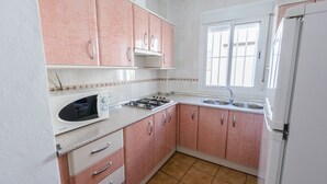 A compact kitchen with pink cabinets, a white countertop, a built-in oven, a gas stove, and a sink. - Casas María Carmona - Casa Tierra Níjar by Ruralidays (Almería)