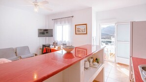 A modern kitchen with a red countertop, a dining area with a table and chairs, a ceiling fan, and a window with a view of mountains. - Casas María Carmona - Casa Luna Níjar by Ruralidays (Almería)