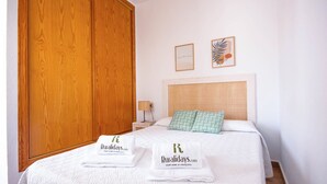 A hotel room with a wooden wardrobe, a bed with white bedding, two pillows, a nightstand with a lamp, and two framed pictures on the wall. - Casas María Carmona - Casa Luna Níjar by Ruralidays (Almería)