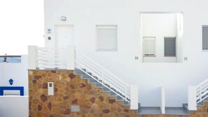 A white building with a stone staircase, a white railing, and numbered doors. - Casas María Carmona - Casa Luna Níjar by Ruralidays (Almería)