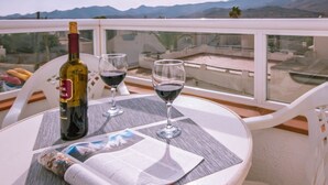 A table with a bottle of wine, two wine glasses, and a menu on a balcony overlooking a mountainous landscape. - Casas María Carmona - Casa Luna Níjar by Ruralidays (Almería)