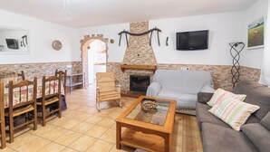 A living room with a stone fireplace, a television mounted on the wall, and a sofa with striped cushions. - Casa Crisal Arriate by Ruralidays (Málaga)