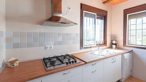 A kitchen with a gas stove, a range hood, a window with blinds, a sink, and a dishwasher. - Casa Crisal Arriate by Ruralidays (Málaga)