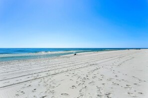 A wide, sandy beach with footprints leading to the water, and a clear blue sky above.