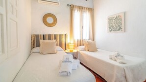 Ett hotellrum med två sängar, en rund spegel, en lampa och ett inramat konstverk föreställande ett löv.