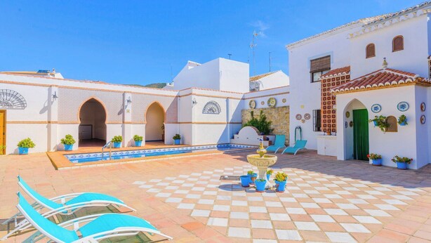 Ein Innenhof mit Pool, Liegestühlen, einer Fontäne und Topfpflanzen.