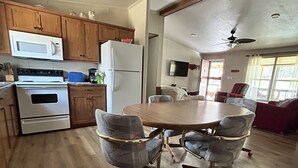 A kitchen with wooden cabinets, a microwave, a refrigerator, and a dining area with a table and chairs.