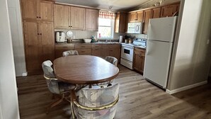 A kitchen with wooden cabinets, a white refrigerator, a stove, a ceiling fan, and a dining table with chairs.